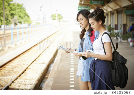 two young female travelers are standing near the railway and looking a map 34205068