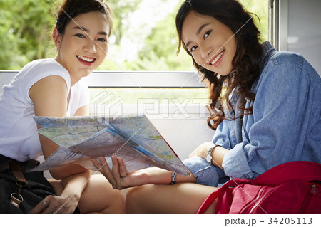 Two happy Asian girls are holding a map and looking at the camera. 34205113