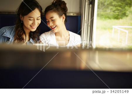 Two Asian girls are sitting on a train, looking at something and smiling. 34205149