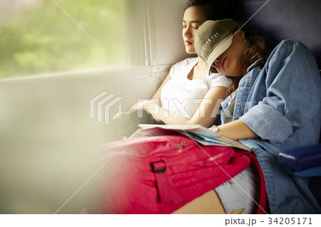 Two young girls are feeling tired when travelling by train. 34205171