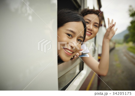 Two Asian women are looking at something from the train and waving hands. 34205175