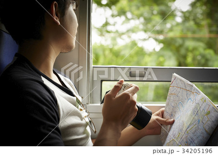 A man is holding a map, a digital camera and looking out of the train. 34205196