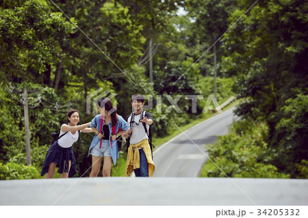 three young asian travellers are joking while walking on a road in forest 34205332