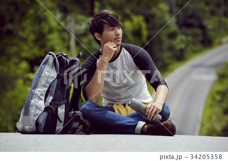 a handsome man with a bottle of water is sitting on the road 34205358