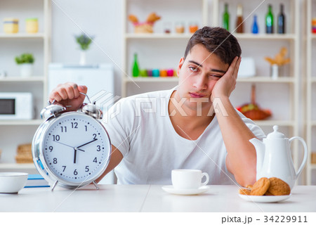 Man with alarm clock falling asleep at breakfast 34229911