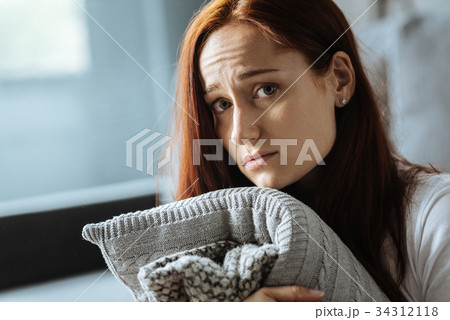 Sad red haired woman holding a cushion 34312118