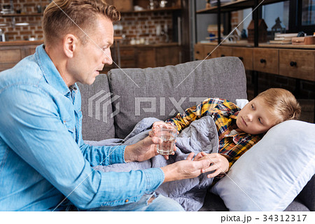 Caring father giving medicine to his ill son Caring father giving medicine to his ill son 34312317