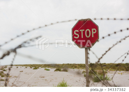 Red stop sign behind safety fence of barbed wire Red stop sign behind safety fence of barbed wire 34337382