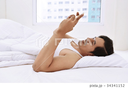 Happy asian man lying down and using mobile phone Happy asian man lying down and using mobile phone 34341152