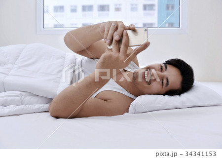 Handsome asian man lying in bed with smartphone Handsome asian man lying in bed with smartphone 34341153