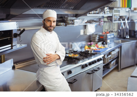 Portrait of smiling chef standing with arms crossed in commercial kitchen 34356562