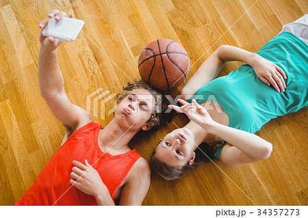 Overhead view of playful friends taking selfie while lying on floor Overhead view of playful friends taking selfie while lying on floor 34357273