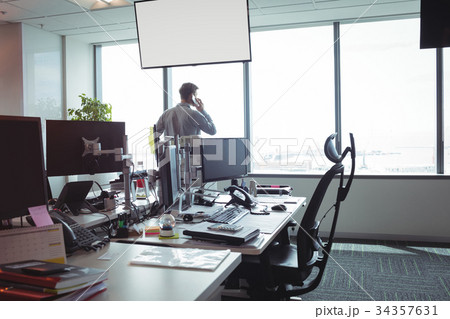 Businessman taking on mobile phone by windows Businessman taking on mobile phone by windows 34357631