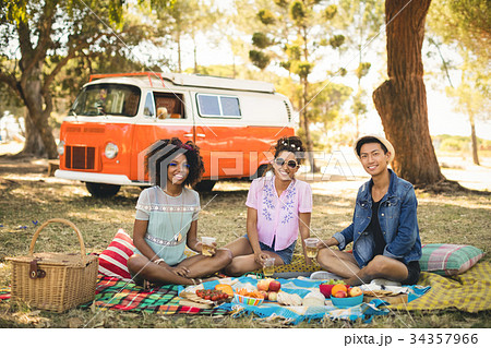 Portrait of smiling friends having food while sitting on picnic blanket Portrait of smiling friends having food while sitting on picnic blanket 34357966