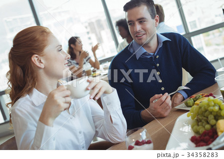 Young business colleagues talking at breakfast table in office Young business colleagues talking at breakfast table in office 34358283