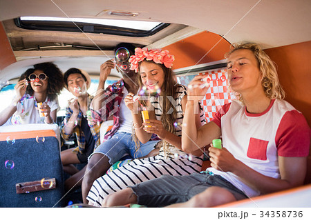 Happy friends blowing bubble wands in camper van Happy friends blowing bubble wands in camper van 34358736