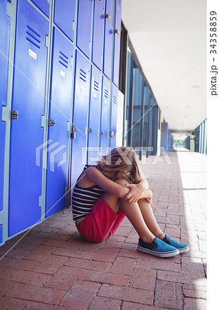 Full length of girl sitting by lockers in corridor 34358859