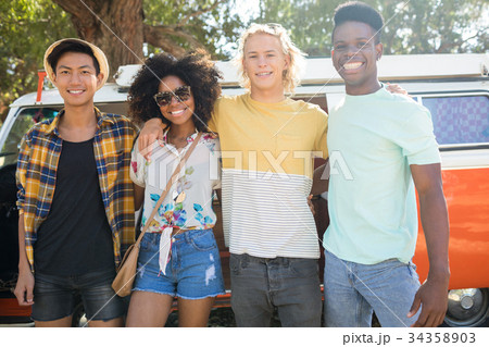 Portrait of smiling friends standing against camper van at campsite 34358903