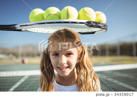 Smiling girl standing below tennis racket and balls 34359017