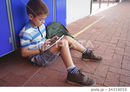 Boy using digital tablet while sitting by locker 34359050
