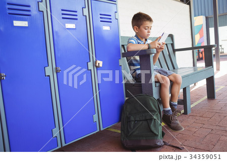 Boy using mobile phone while sitting on bench by lockers 34359051