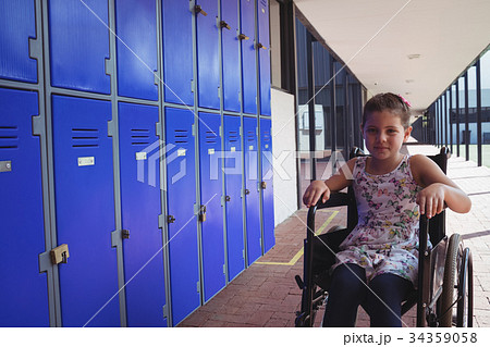 Portrait of schoolgirl sitting on wheelchair by lockers 34359058