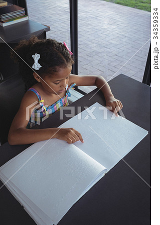 Girl reading braille at desk in library 34359334