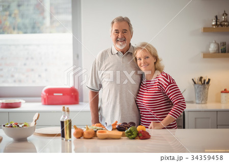 Smiling senior couple standing together in kitchen Smiling senior couple standing together in kitchen 34359458