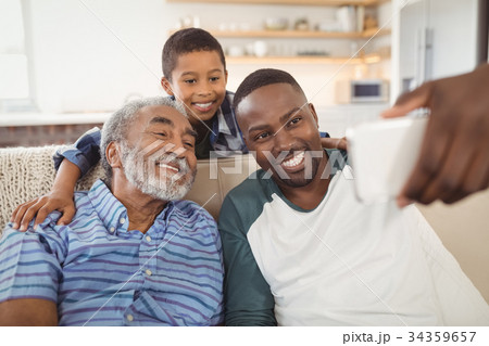 Smiling multi-generation family taking selfie from mobile phone in living room Smiling multi-generation family taking selfie from mobile phone in living room 34359657