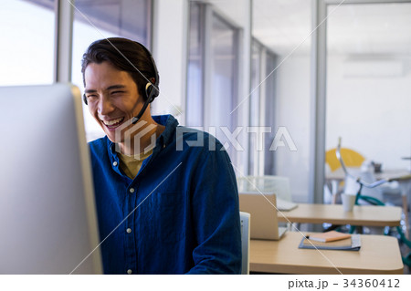Male executive in headset working over computer at his desk Male executive in headset working over computer at his desk 34360412