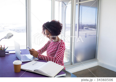 Female executive using mobile phone while working over laptop Female executive using mobile phone while working over laptop 34360506