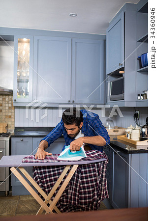 Man ironing shirt while standing in kitchen 34360946