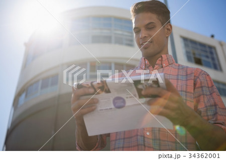 Young man reading paper while standing by building 34362001
