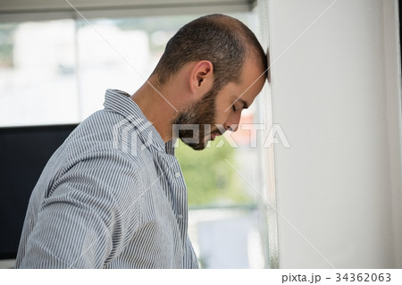 Frustrated designer leaning on wall at office Frustrated designer leaning on wall at office 34362063