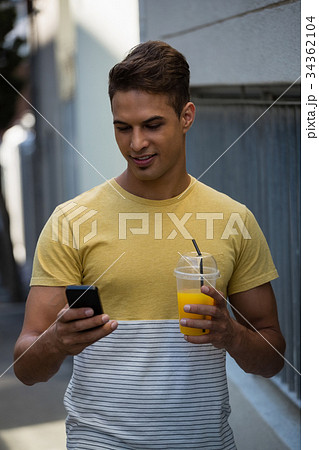 Smiling young man having juice while using mobile phone 34362104