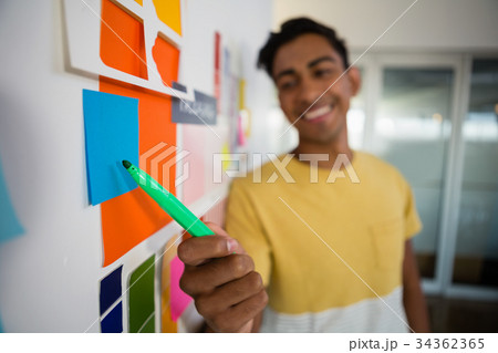 Smiling man pointing at sticky notes with felt tip pen in office 34362365