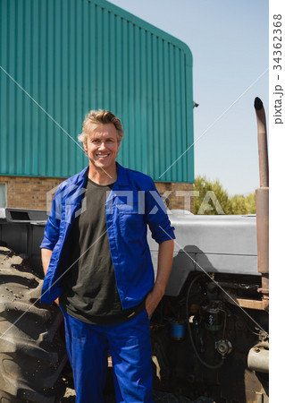 Worker standing with hands in pocket near tractor Worker standing with hands in pocket near tractor 34362368