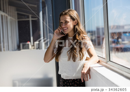 Smiling businesswoman talking on phone while standing by window 34362605
