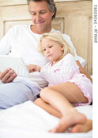 Smiling father and daughter using digital tablet on bed Smiling father and daughter using digital tablet on bed 34363061