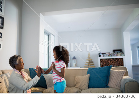 Granddaughter and grandmother playing clapping games on sofa in living room Granddaughter and grandmother playing clapping games on sofa in living room 34363736