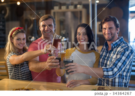 Portrait of happy friends toasting beer at table in bar 34364267