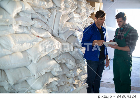 Coworkers discussing while standing barley sacks Coworkers discussing while standing barley sacks 34364324