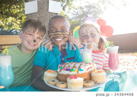 Happy children with face paint having food and drinks at park 34364408