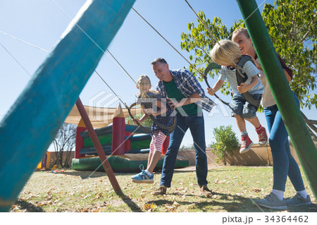 Playful parents swinging children at playground 34364462