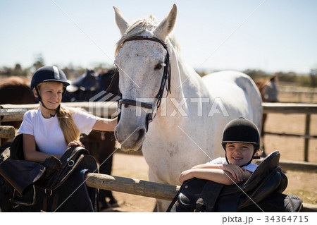 Two girls standing next to the white horse in the ranch 34364715