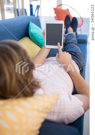 Male executive using digital tablet while relaxing on sofa 34365122