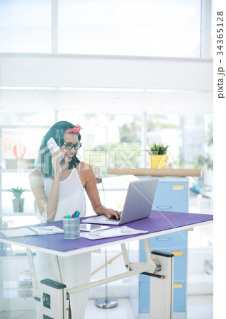 Executive talking on mobile phone while using laptop in office Executive talking on mobile phone while using laptop in office 34365128