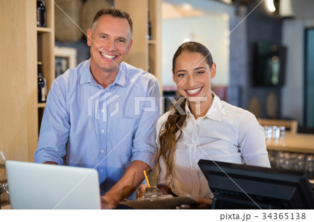 Smiling manager and bartender standing at bar counter Smiling manager and bartender standing at bar counter 34365138