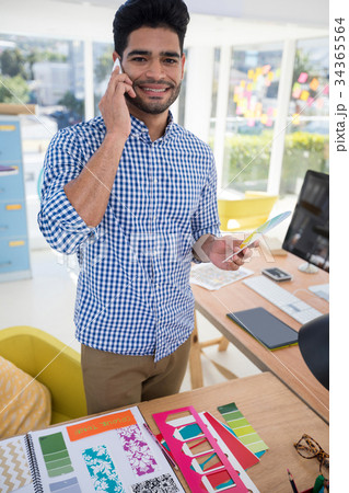 Male graphic designer talking on mobile phone at desk 34365564
