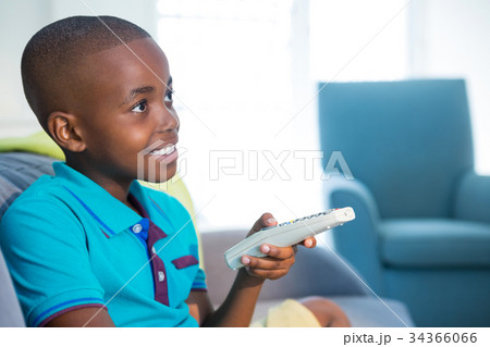 Smiling boy holding remote control on sofa at home Smiling boy holding remote control on sofa at home 34366066